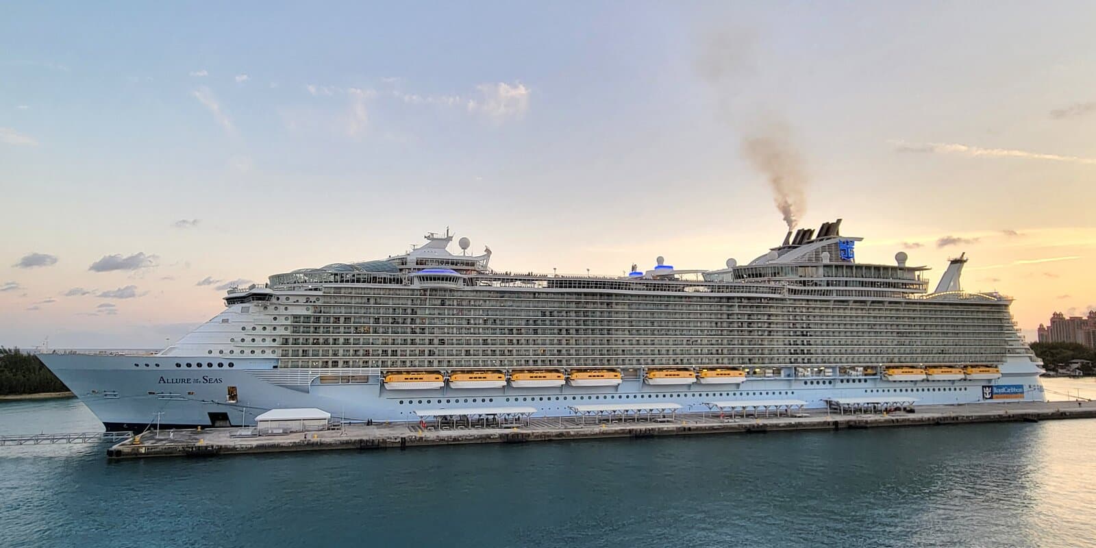 Allure of the Seas docked at Nassau Cruise Port at sunset, with the ship name on the bow and yellow lifeboats along the hull