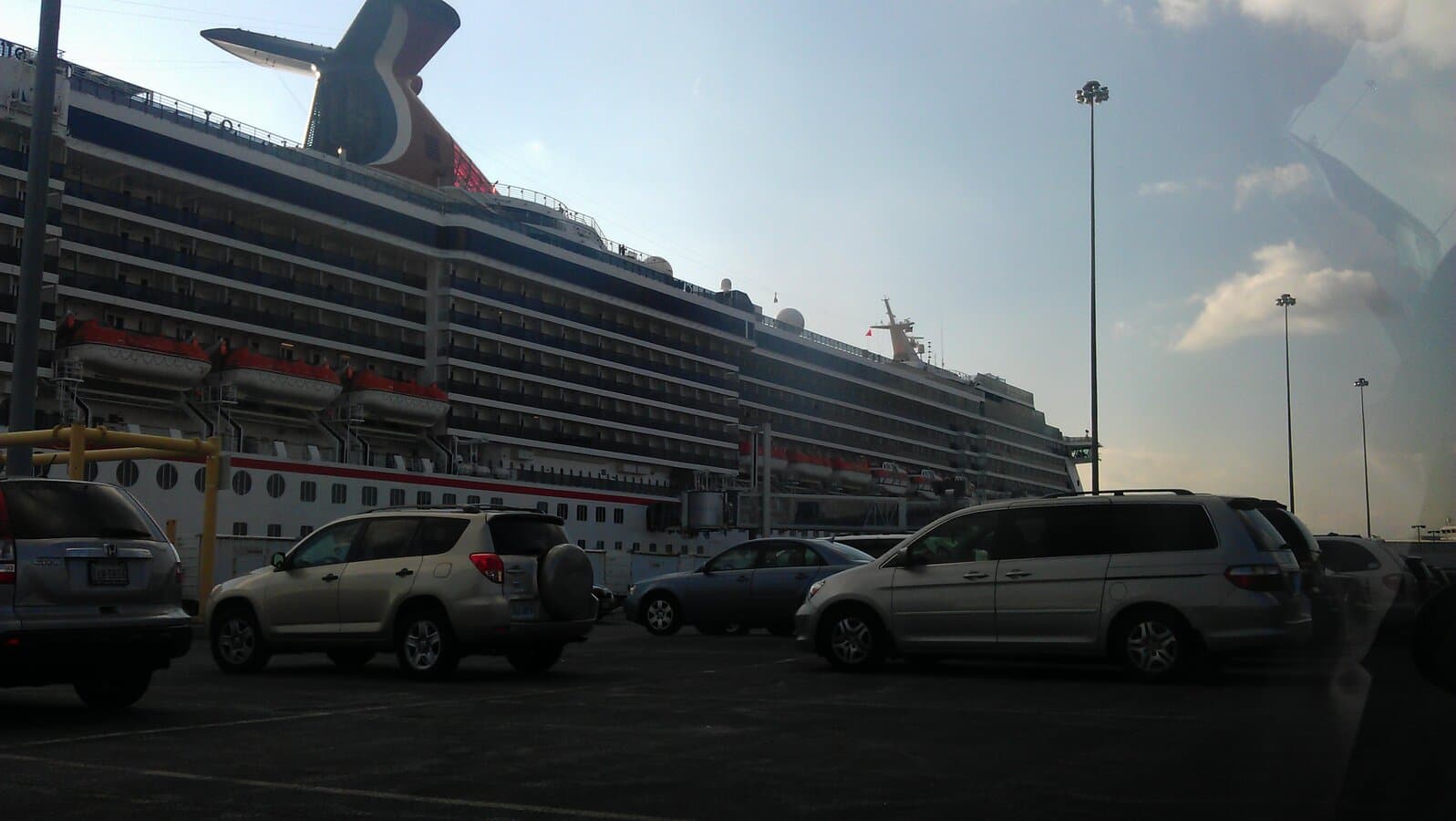 Carnival Pride docked at the Baltimore cruise terminal with the ship's whale-tail funnel and passenger parking in the foreground