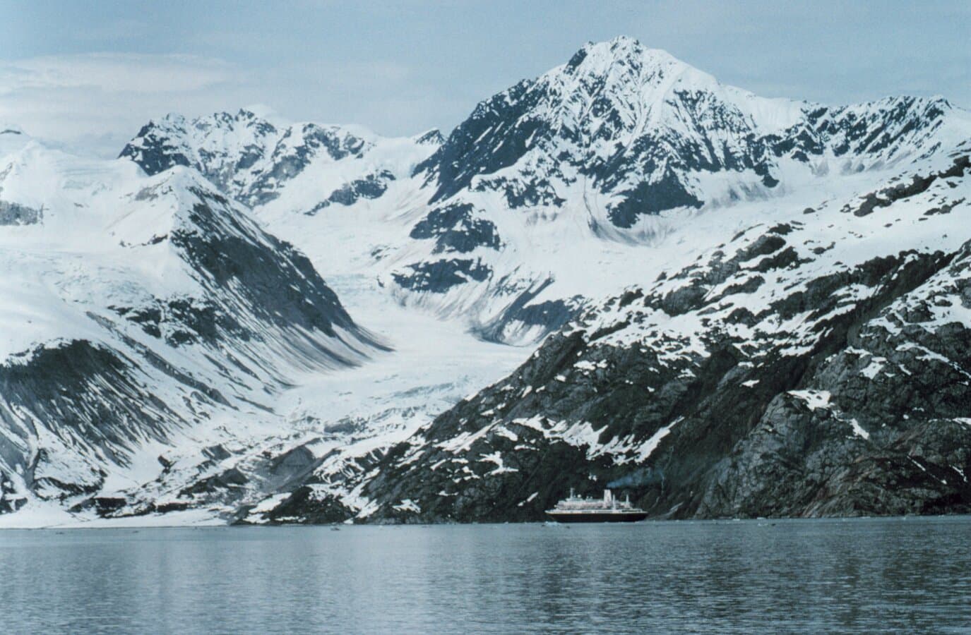 Cruise ship in the distance below towering Glacier Bay ice walls and forested mountains
