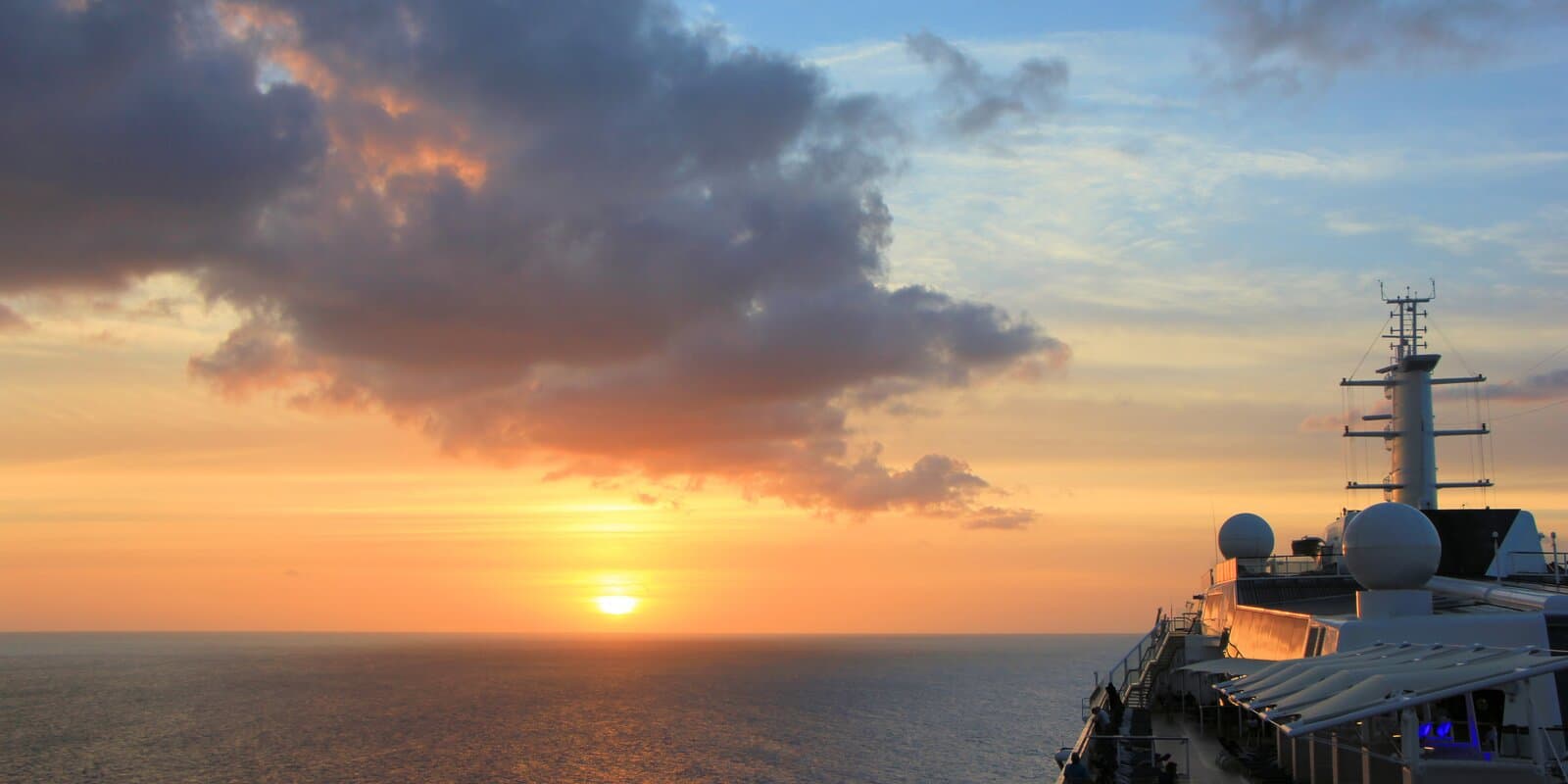 Sunrise over the Caribbean Sea with dramatic clouds and part of a cruise ship's upper deck visible on the right