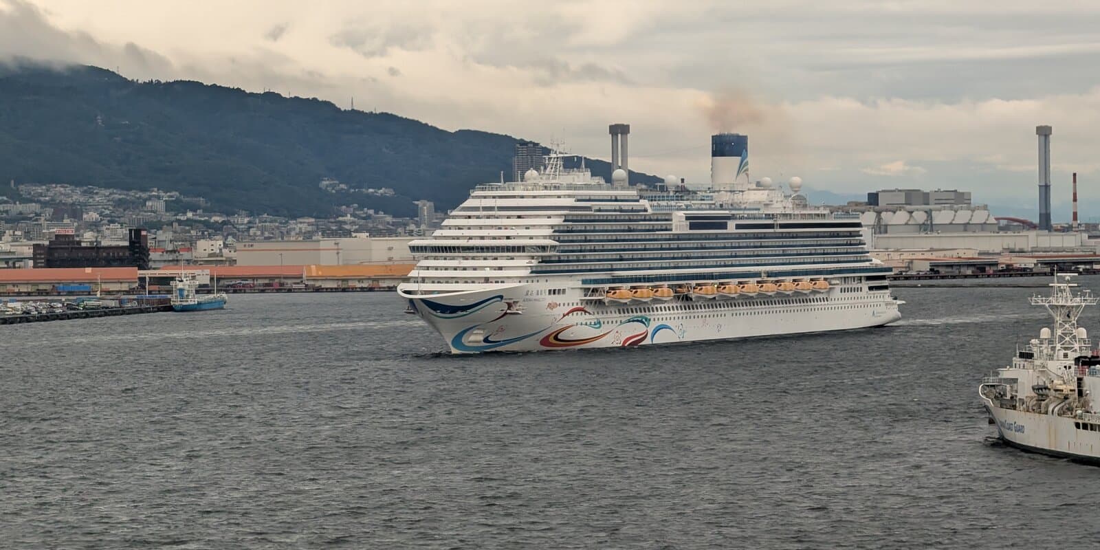Adora Magic City cruise ship at Kobe port — white hull with blue, red, and yellow bow graphics