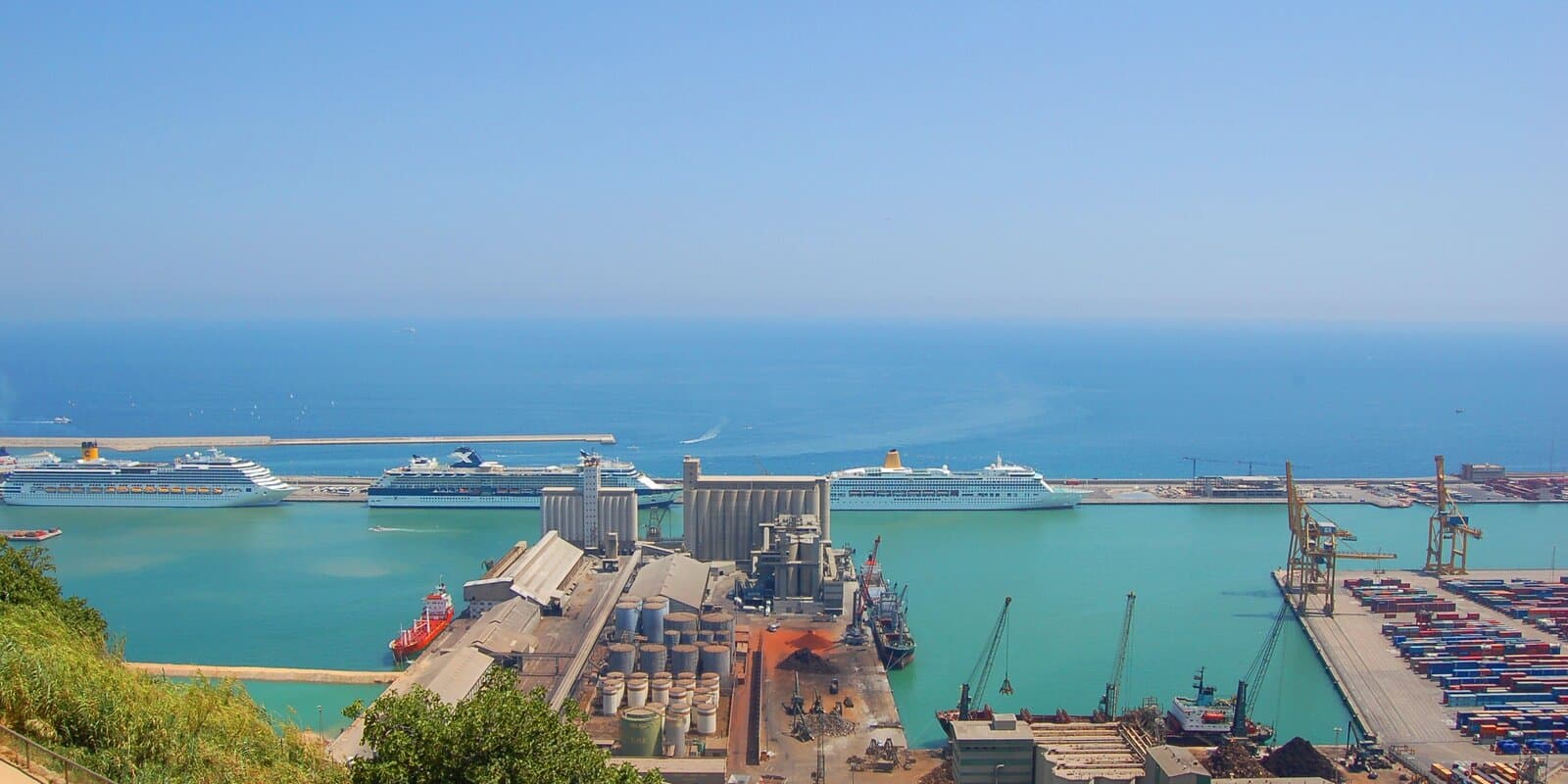 Elevated view of Barcelona's cruise ship terminal with three large cruise ships docked along the pier and port infrastructure in the foreground