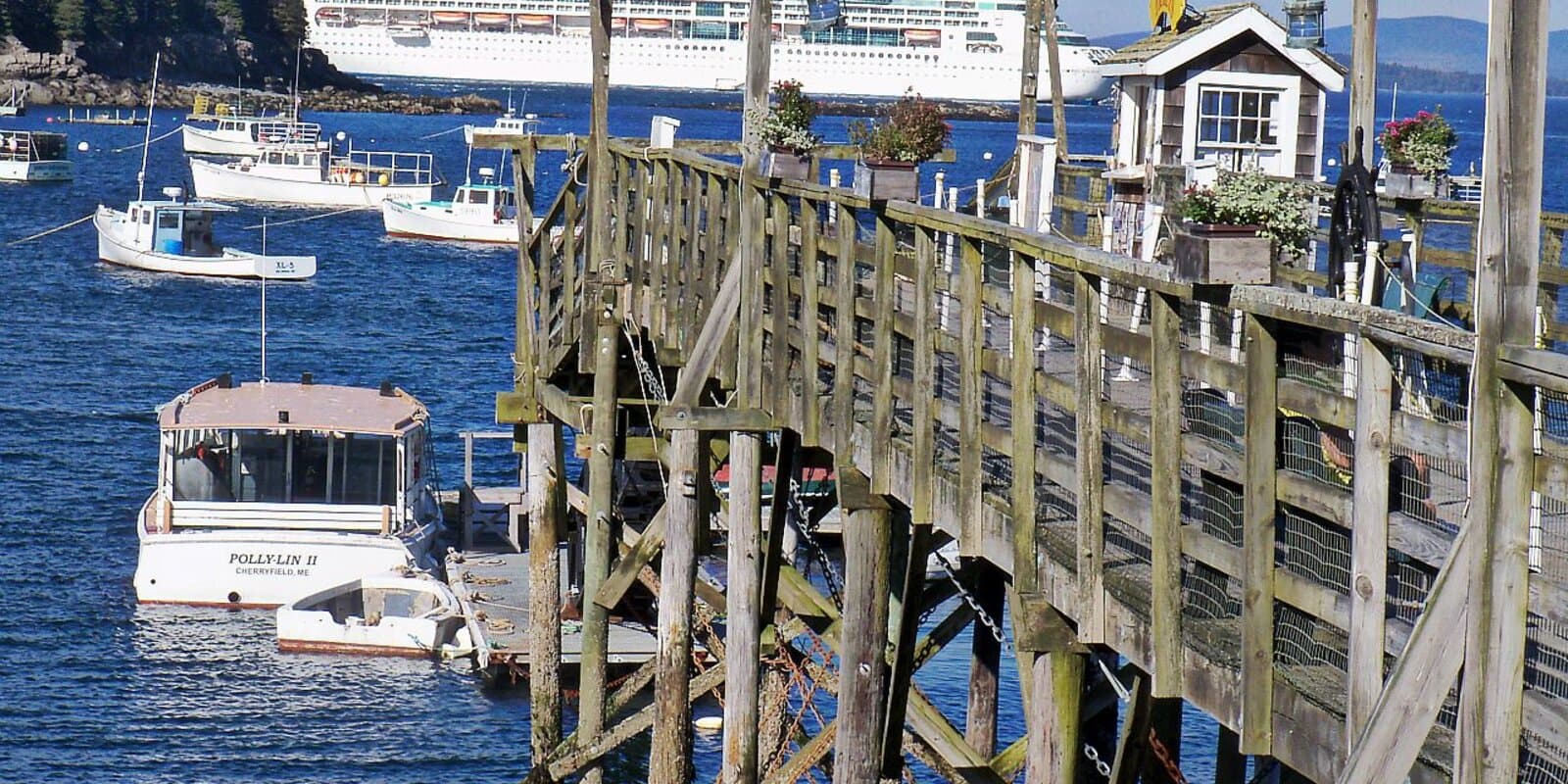 Cruise ship anchored in Frenchman Bay off Bar Harbor, Maine, with fishing boats and a wooden pier in the foreground