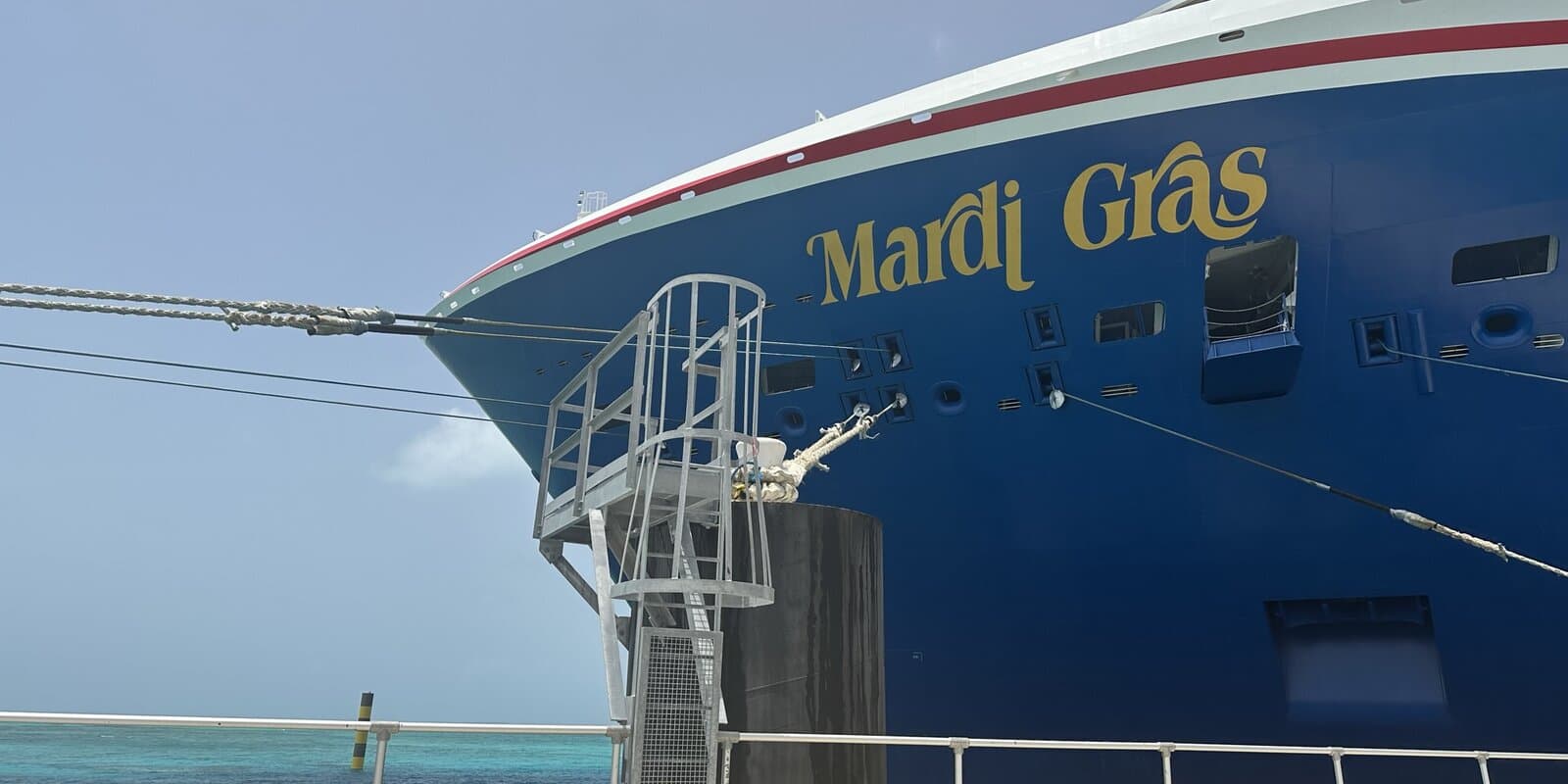 Carnival Mardi Gras cruise ship docked at a pier, with the ship name visible on the blue hull and mooring lines secured to the dock