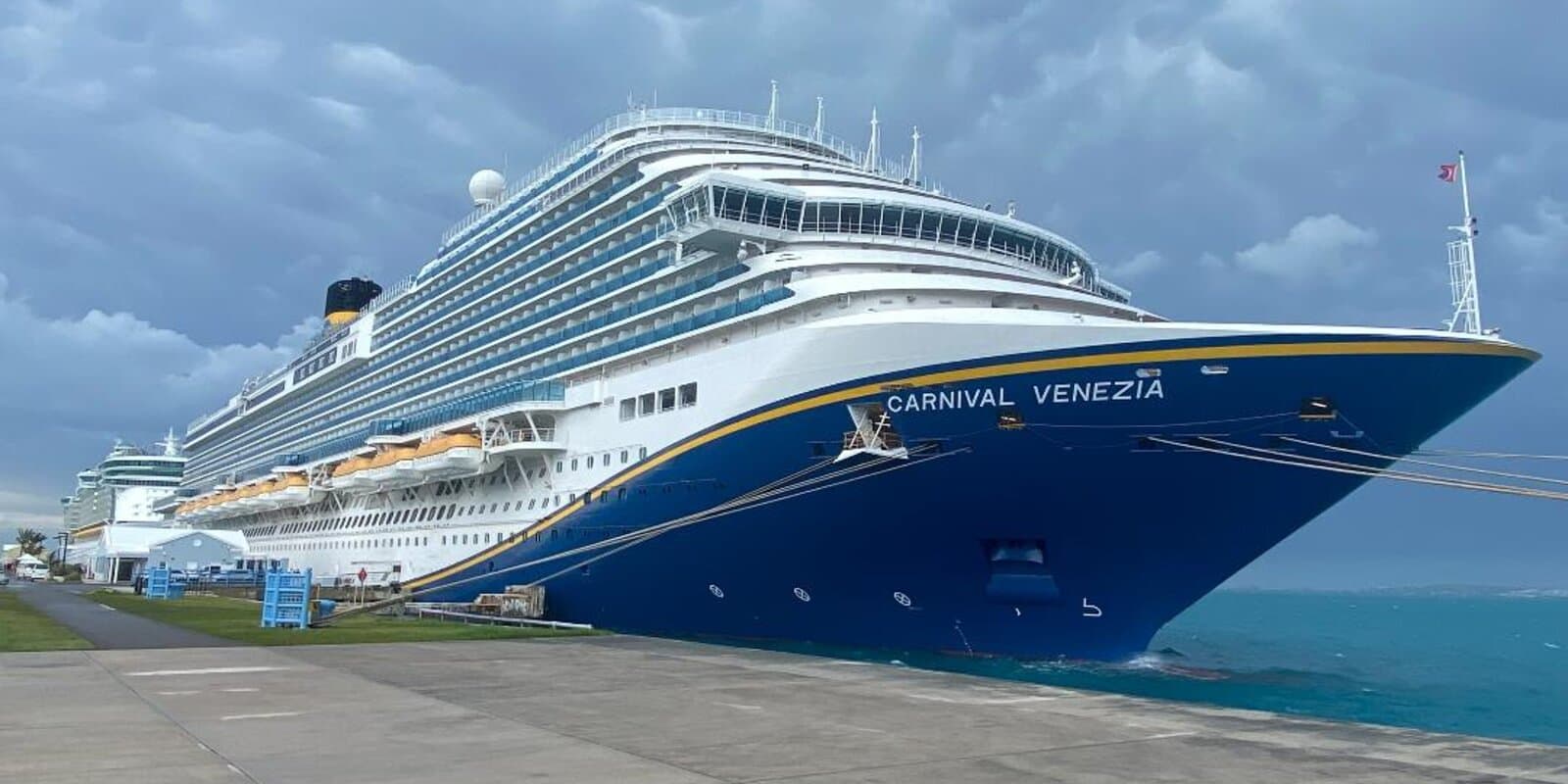 Carnival Venezia cruise ship bow at a pier with turquoise water and dark storm clouds overhead