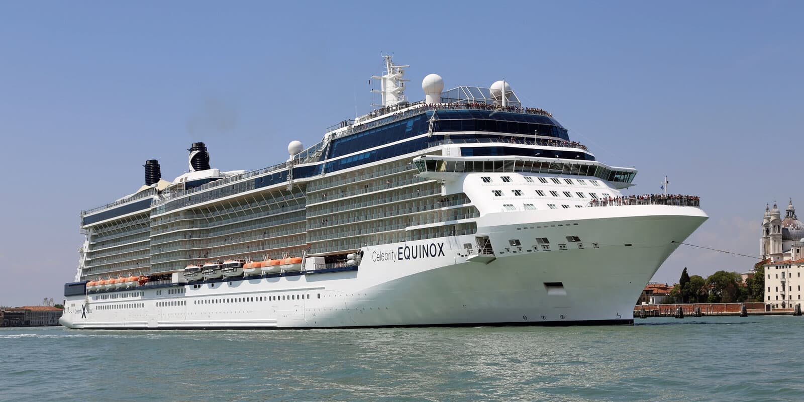 Celebrity Equinox cruise ship with hull name visible, sailing past historic waterfront buildings in Venice harbor