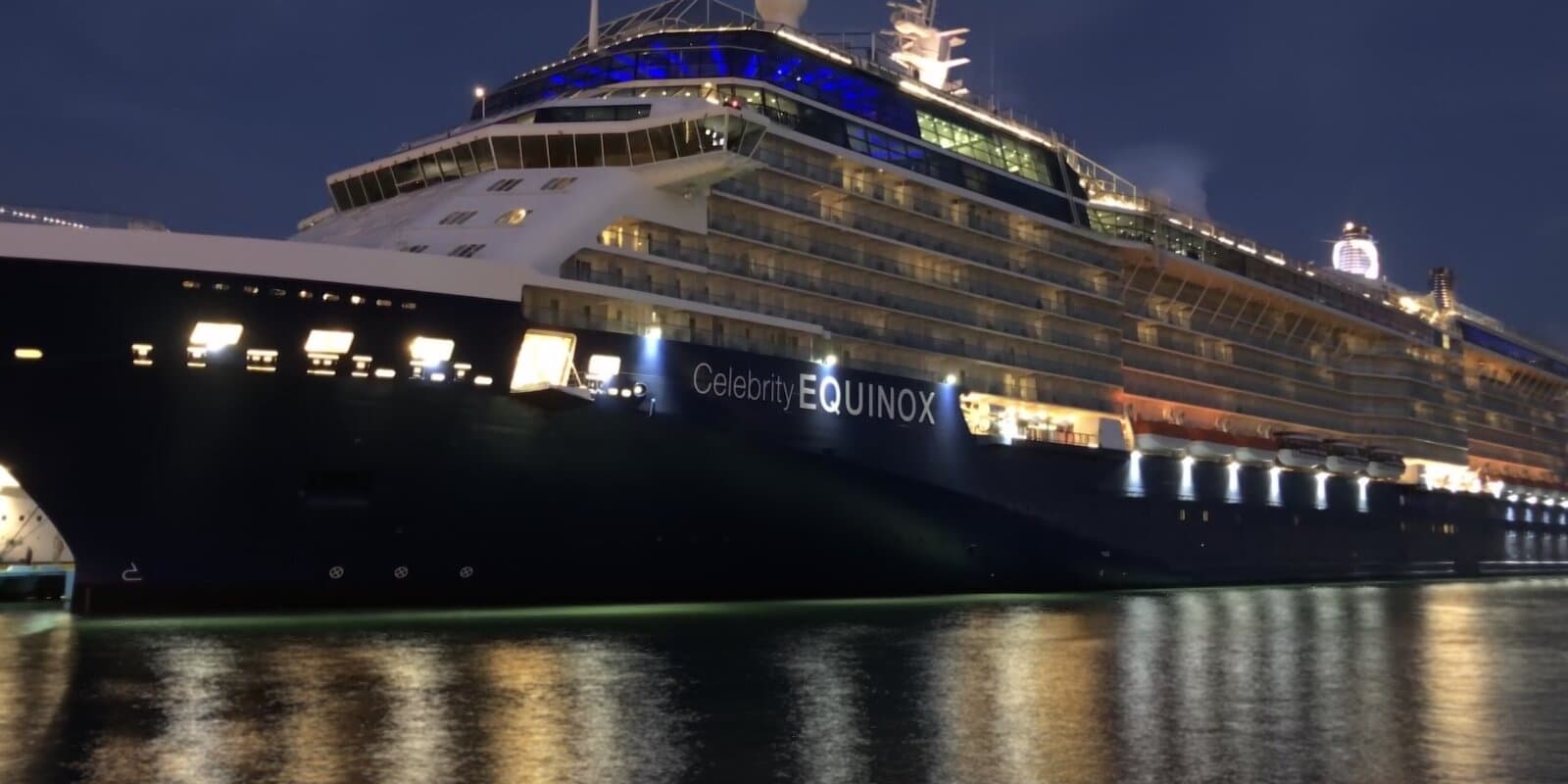 Celebrity Equinox cruise ship docked at a pier at night in San Juan, Puerto Rico, with hull lettering and deck lights reflected on the water