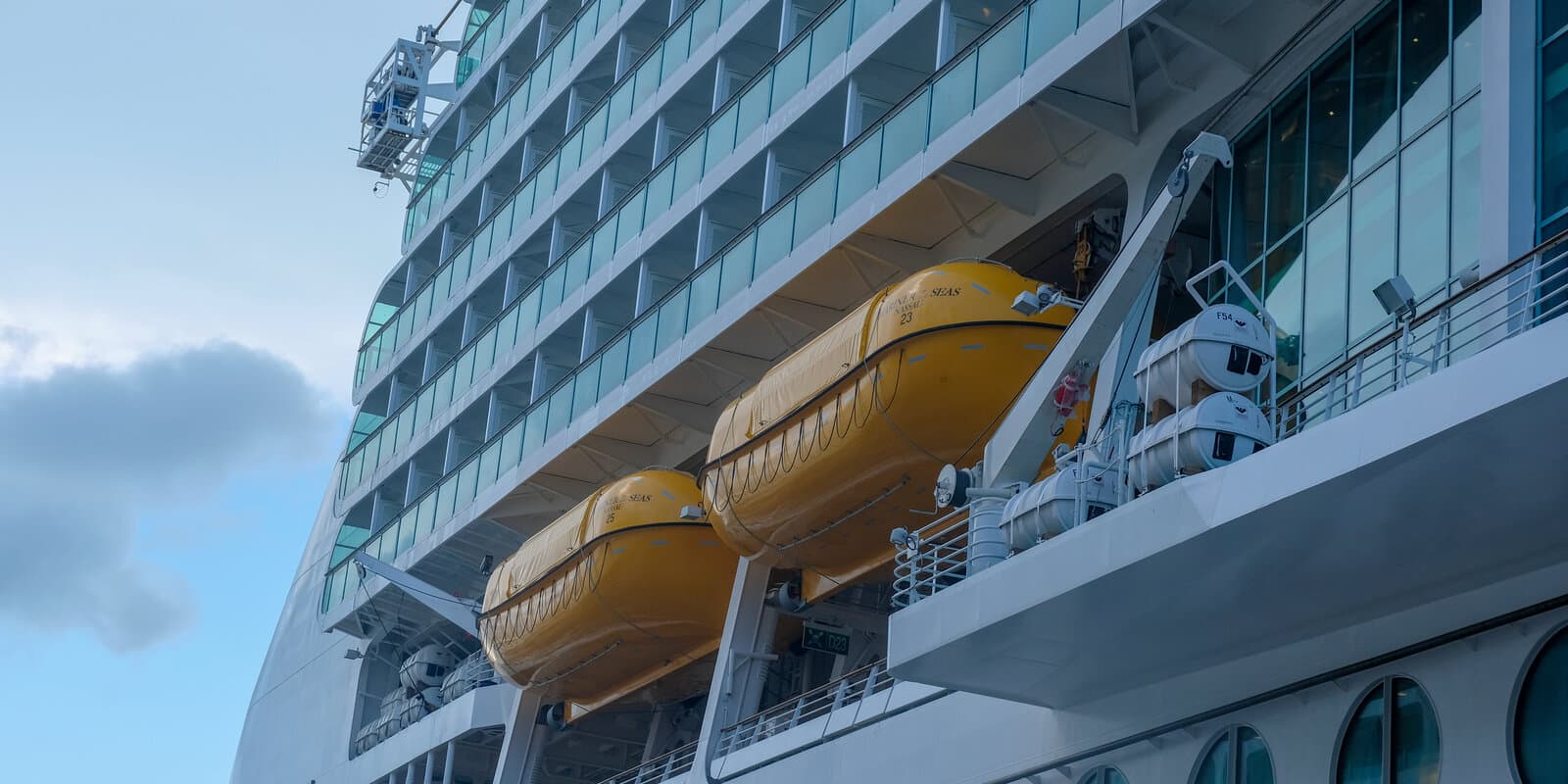 Multiple decks of balcony staterooms on the side of a large cruise ship, with yellow lifeboats along the hull