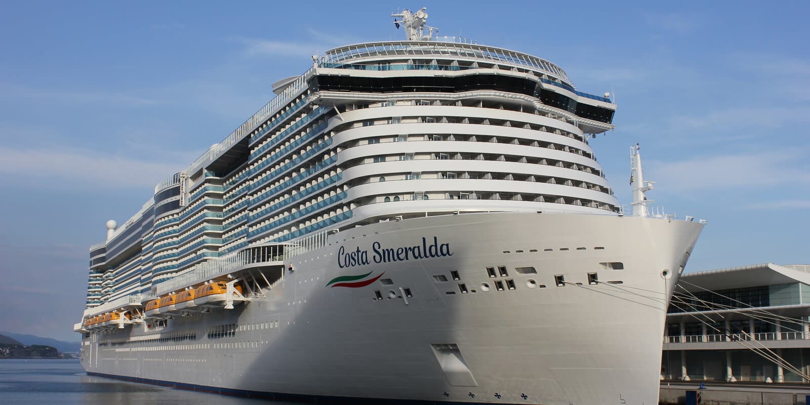 Costa Smeralda cruise ship docked at Savona with yellow Costa funnel, white hull, and port terminal buildings behind
