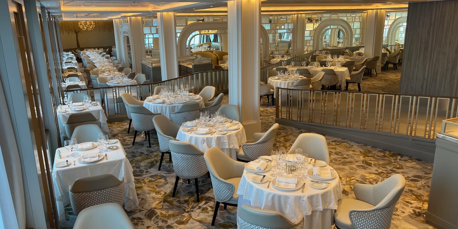 Empty main dining room on a cruise ship with formal place settings, white tablecloths, and elegant seating
