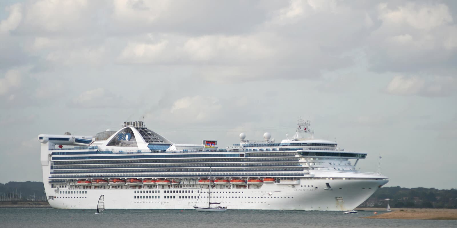 Grand Princess cruise ship with a large outdoor screen visible on the upper deck, sailing on calm water