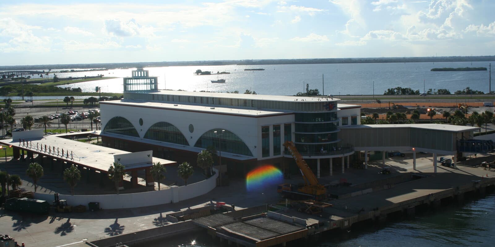 Cruise ship docked at a white port terminal building with pier walkways and palm trees