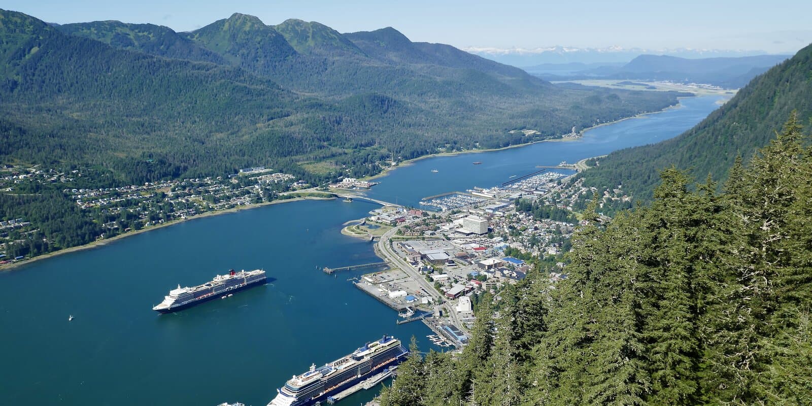 Cunard Queen Elizabeth at Juneau, Alaska with the ship's black hull, white superstructure, and red funnel visible against forested mountains