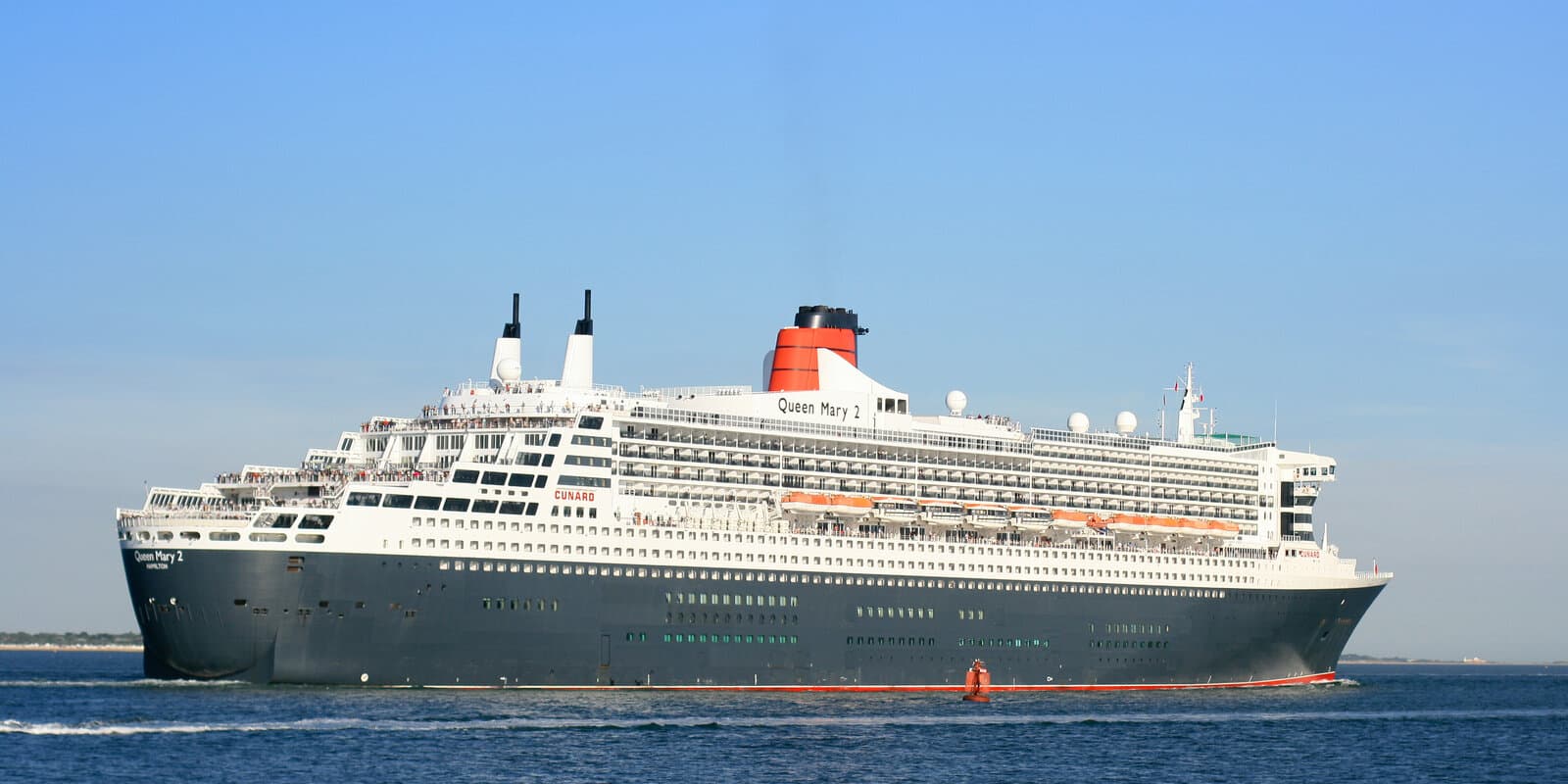 Queen Mary 2 outbound on Southampton Water with black hull, white superstructure, and Cunard red funnel, seen from the starboard quarter