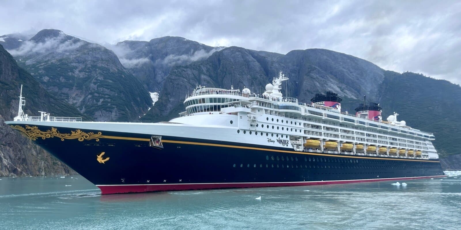 Disney Wonder cruise ship in a misty Alaska fjord with glacier-topped mountains and ice floes in the water