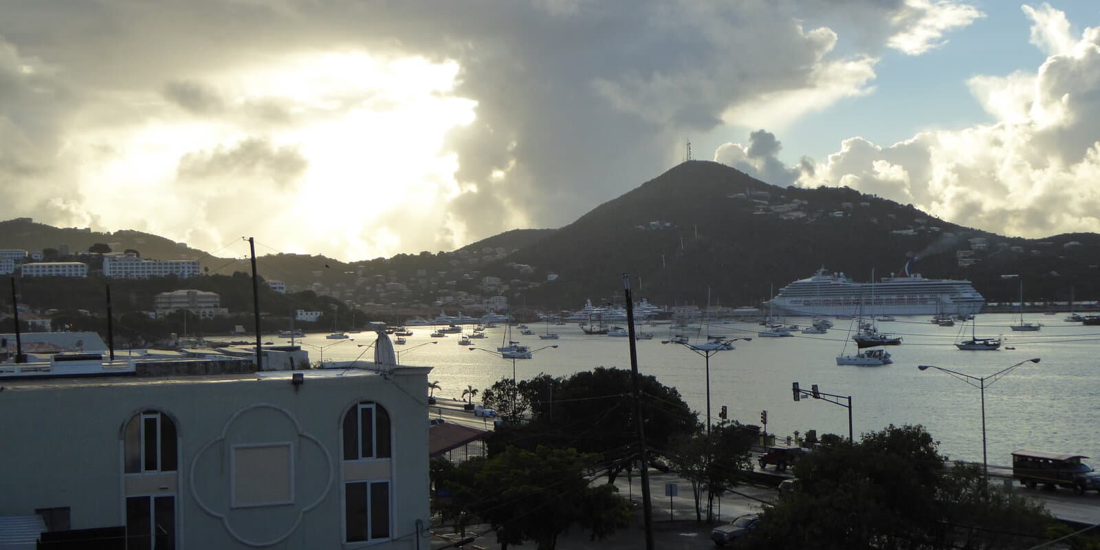 Charlotte Amalie harbor in St. Thomas with a cruise ship docked and sailboats moored in the bay, green hills surrounding the port under a partly cloudy sky