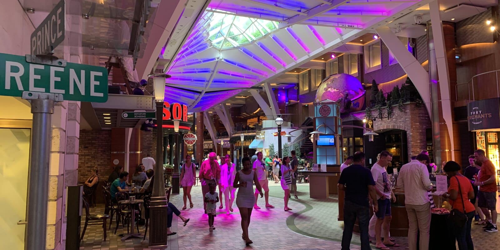 Interior view of the Royal Promenade on Royal Caribbean's Oasis of the Seas, with shops, seating, and passengers in a bright multi-deck atrium.