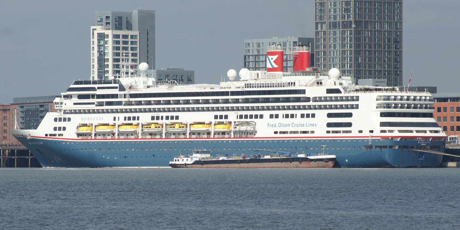 A cruise ship moored at a terminal pier with city buildings in the background