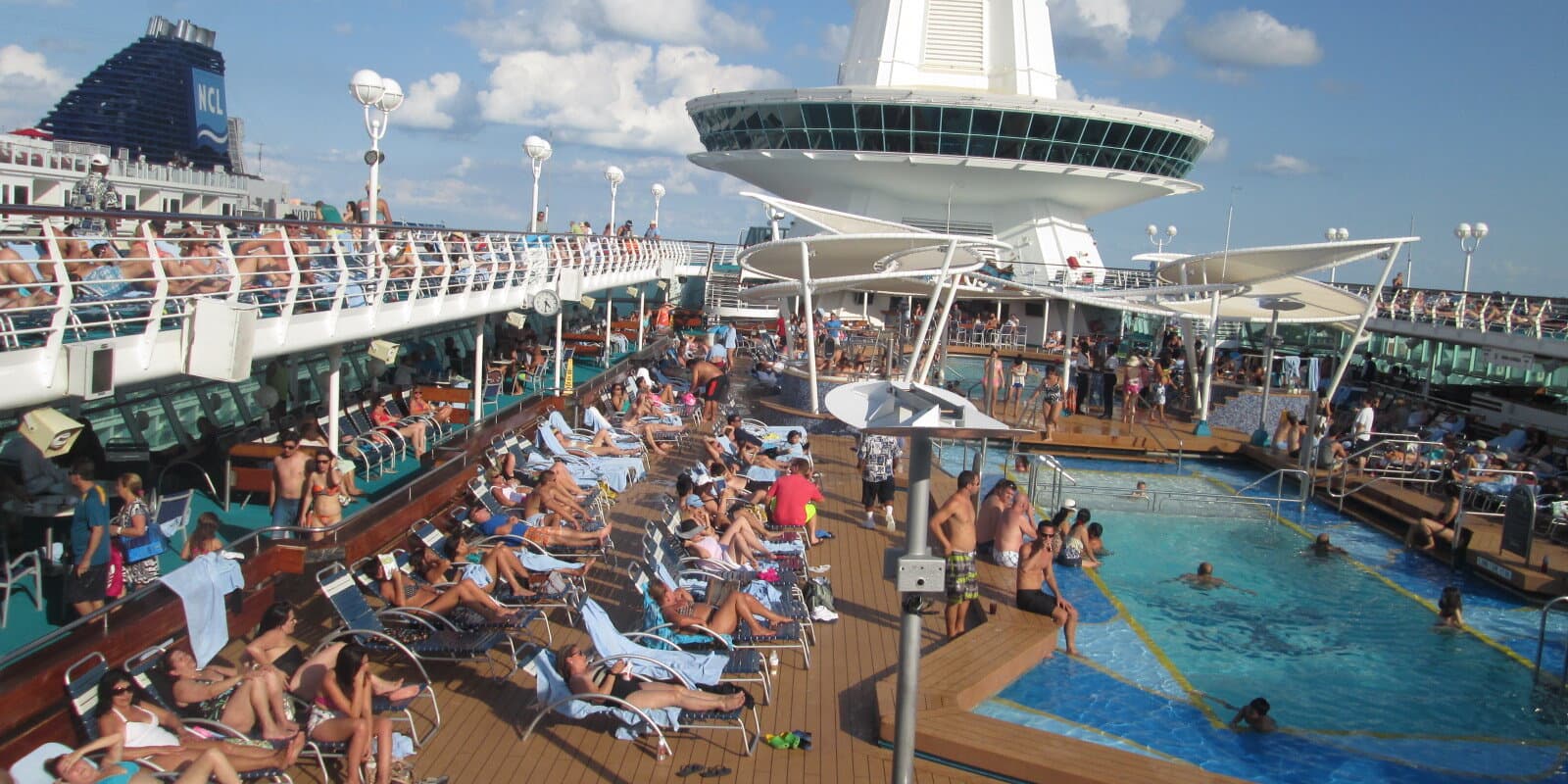 Cruise ship pool deck with lounge chairs and swimmers on a sunny day
