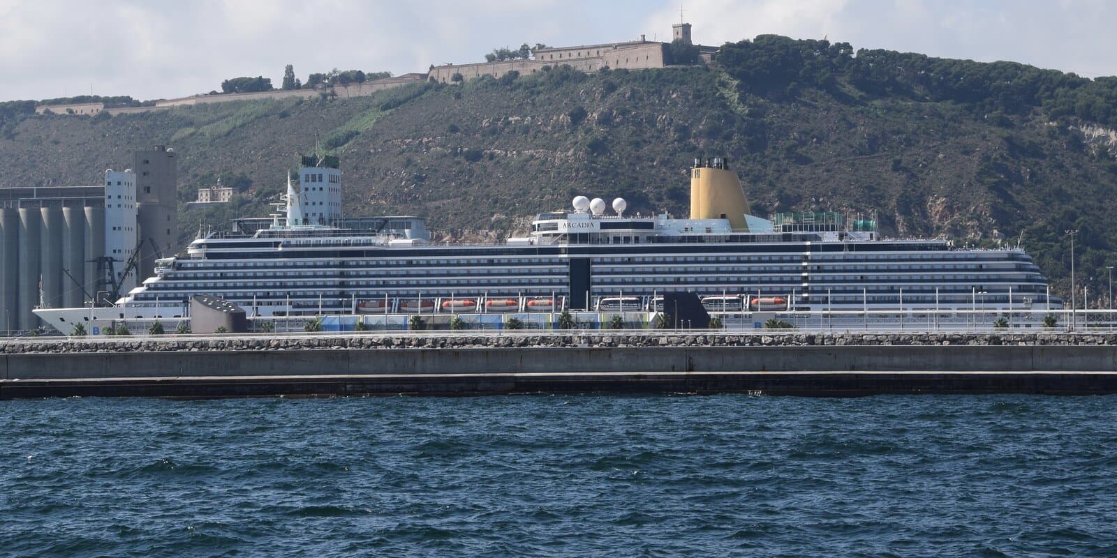 MS Arcadia cruise ship docked at the Port of Barcelona pier with city buildings in the background