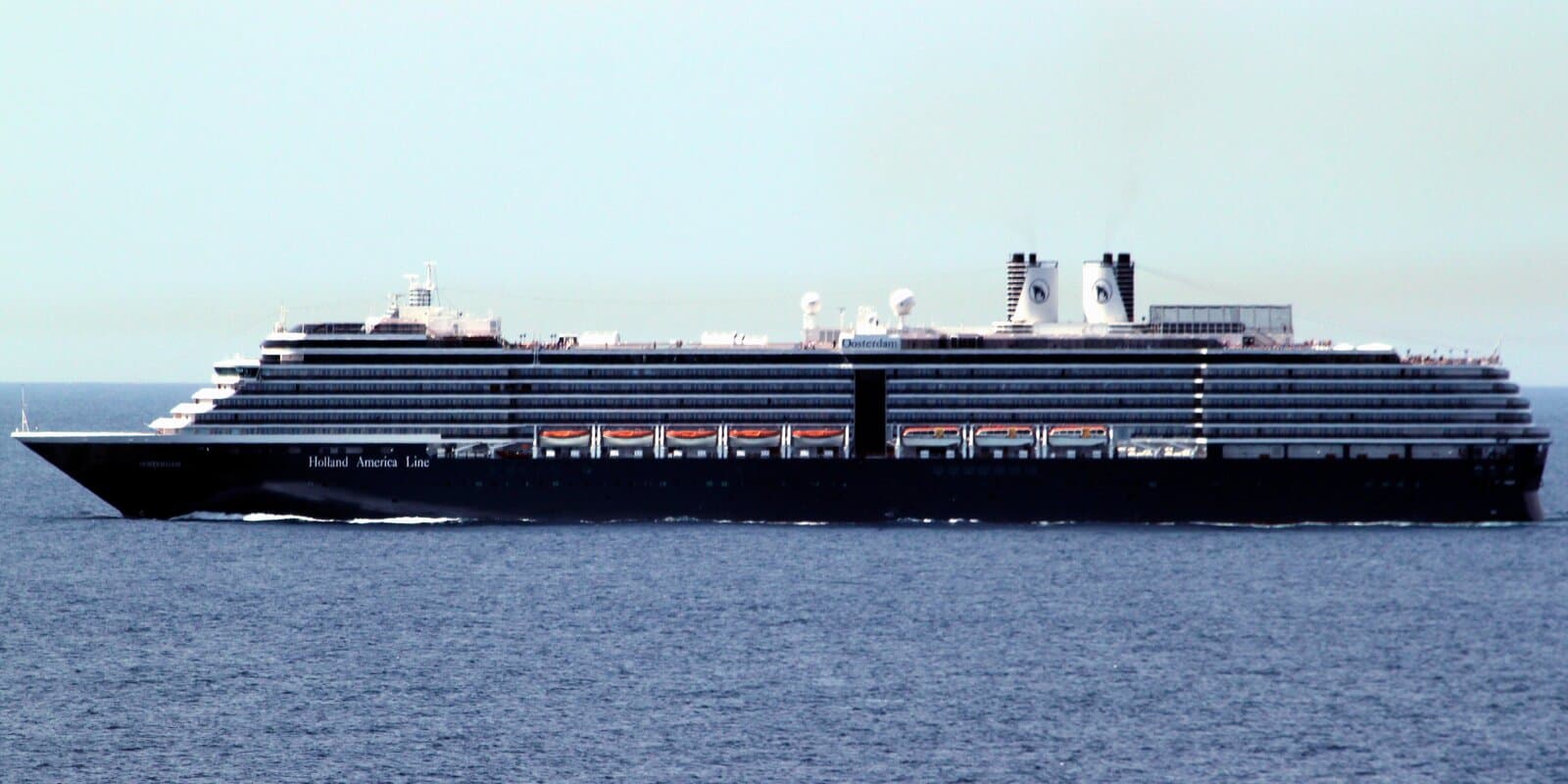 Holland America Line cruise ship Oosterdam in side profile at sea, with dark blue hull, white superstructure, and twin funnels bearing the line's sailing-ship logo.