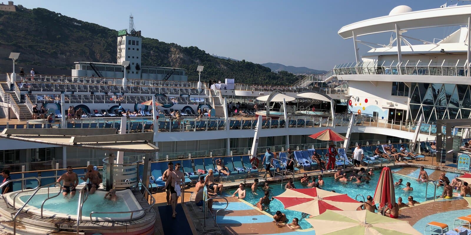 Pool deck on Oasis of the Seas with passengers swimming and lounging on blue chairs under a sunny sky