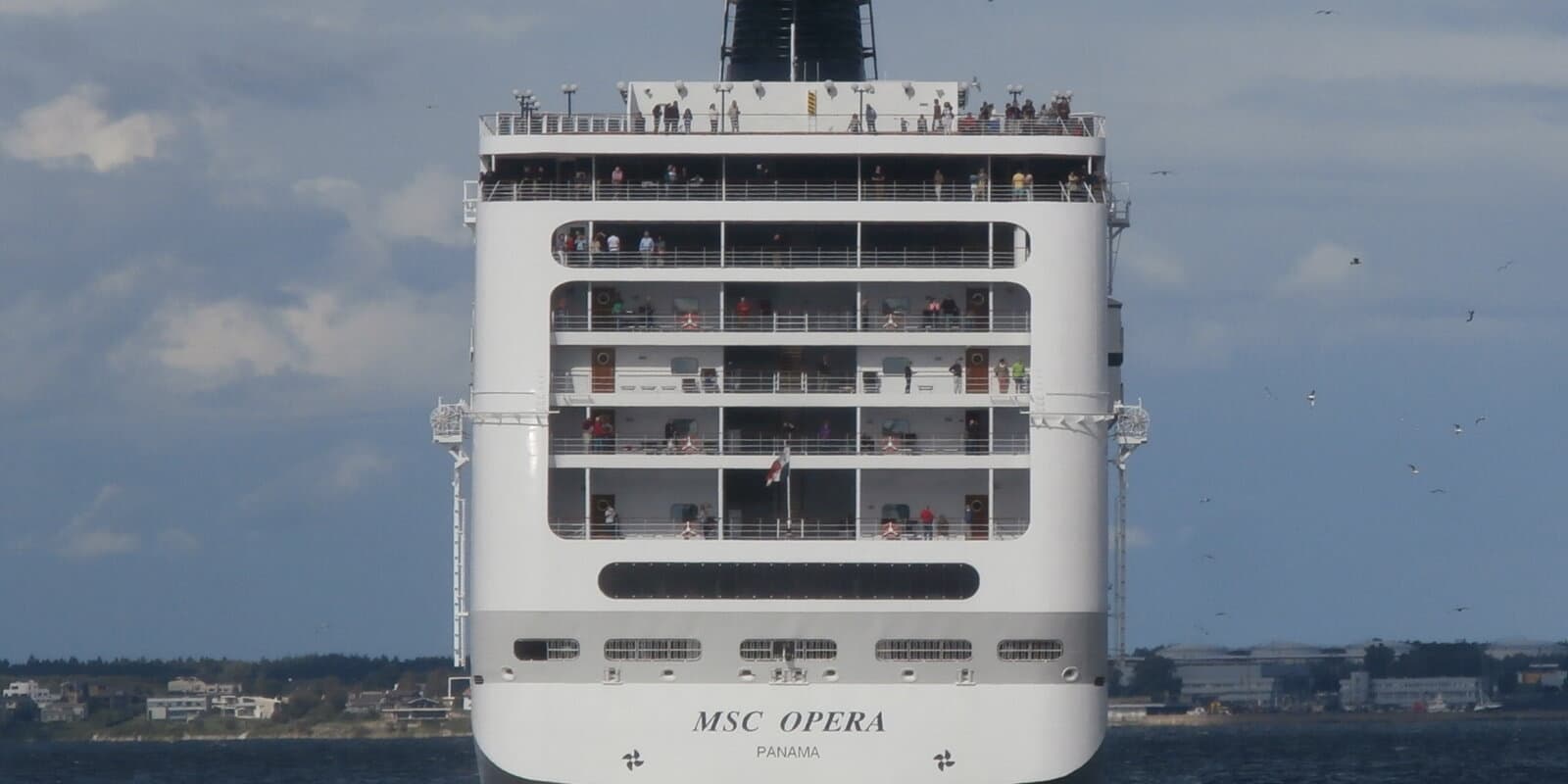 MSC Opera cruise ship stern at sea, with passengers on upper decks and the ship name visible on the hull