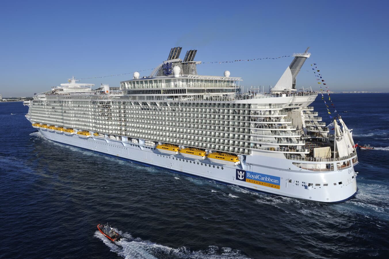 Oasis of the Seas under Coast Guard escort approaching Port Everglades, Florida, with the ship name visible on the stern and blue ocean in the foreground