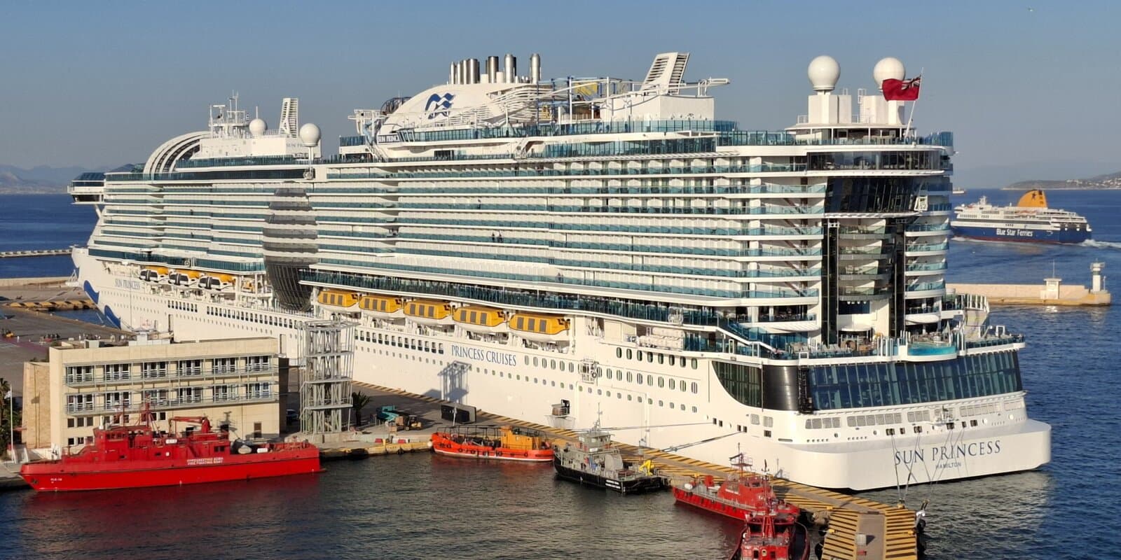 Sun Princess cruise ship docked at Piraeus Harbour, Greece, with white hull, blue Sea Witch funnel, and glass dome visible from the stern