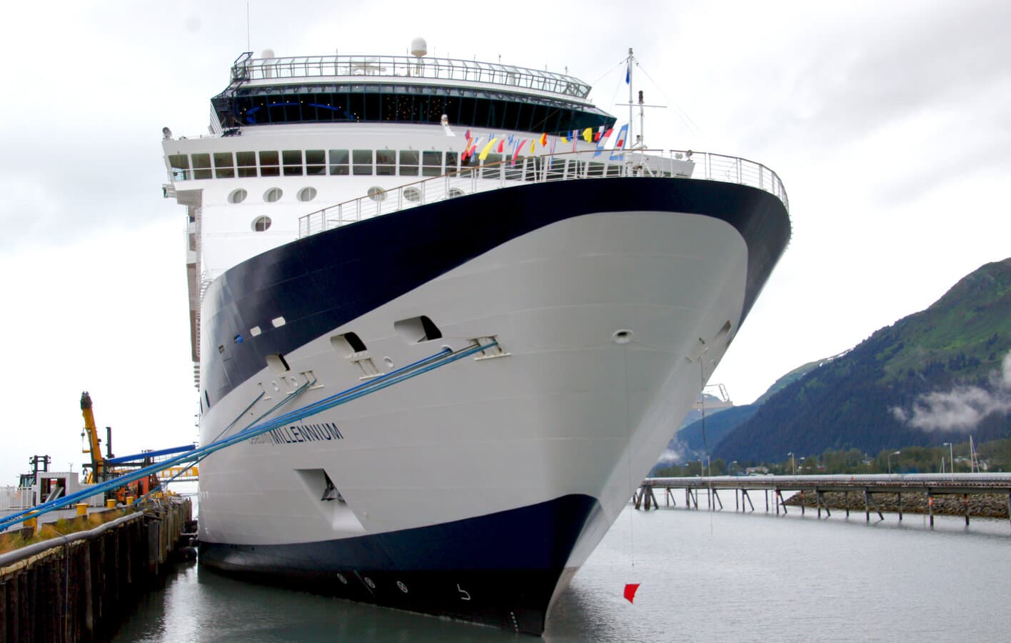 Celebrity Millennium cruise ship docked at Seward, Alaska, with forested Kenai mountains rising behind Resurrection Bay