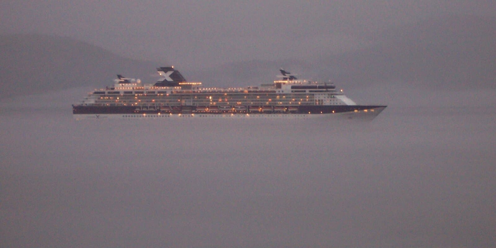 Cruise ship sailing through misty Alaska Inside Passage waters with forested coastal mountains along the shoreline