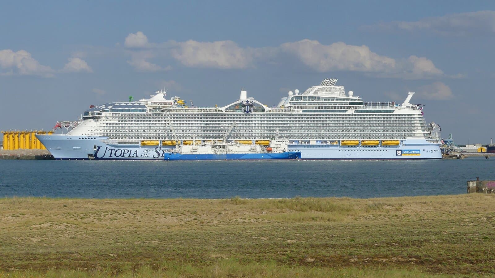 Utopia of the Seas docked at La Rochelle-Pallice harbor, France, with the ship's name on the hull and a service vessel alongside