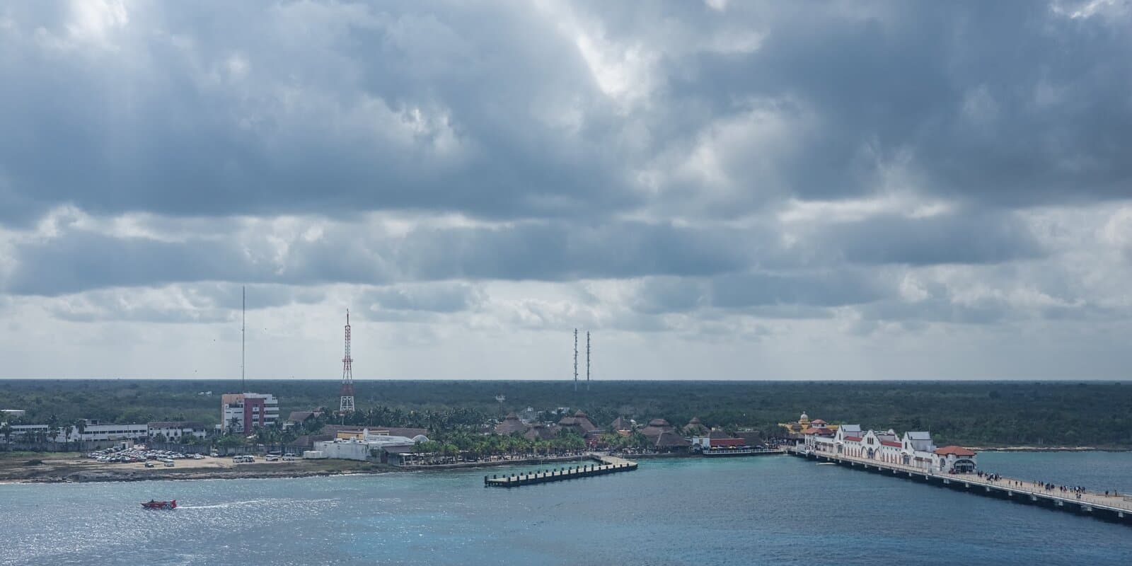 Cozumel cruise port viewed from a ship deck, with a pier extending into turquoise water and a coastal town under a cloudy sky