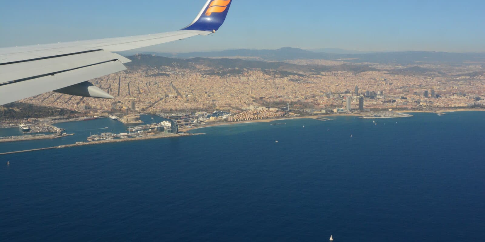 Aerial view of Barcelona's Mediterranean coastline with cruise ship terminals along the waterfront, photographed from an airplane over the sea