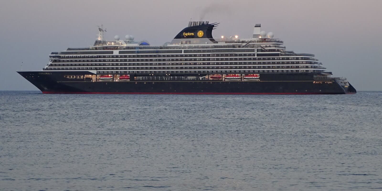 Explora I, a sister ship to Explora III, underway at dusk with a dark hull, red lifeboats, and white balconied decks
