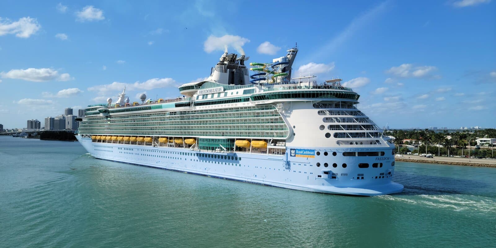 Freedom of the Seas underway near Port Miami, stern three-quarter view with yellow lifeboats and turquoise water