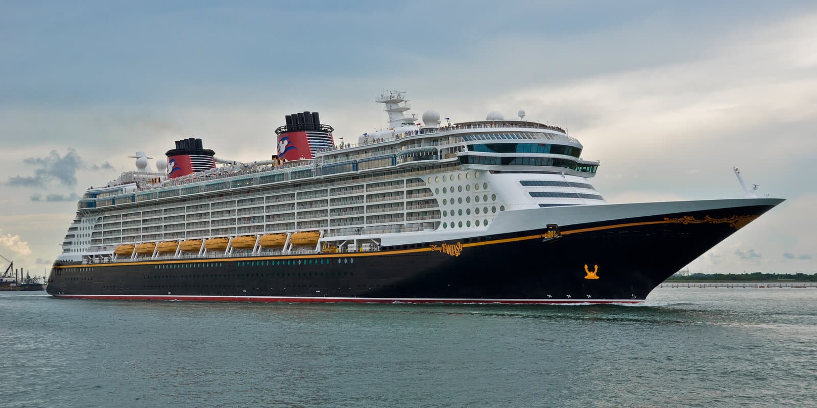 Disney Fantasy cruise ship underway near Port Canaveral, black hull with red Mickey Mouse funnels and yellow lifeboats