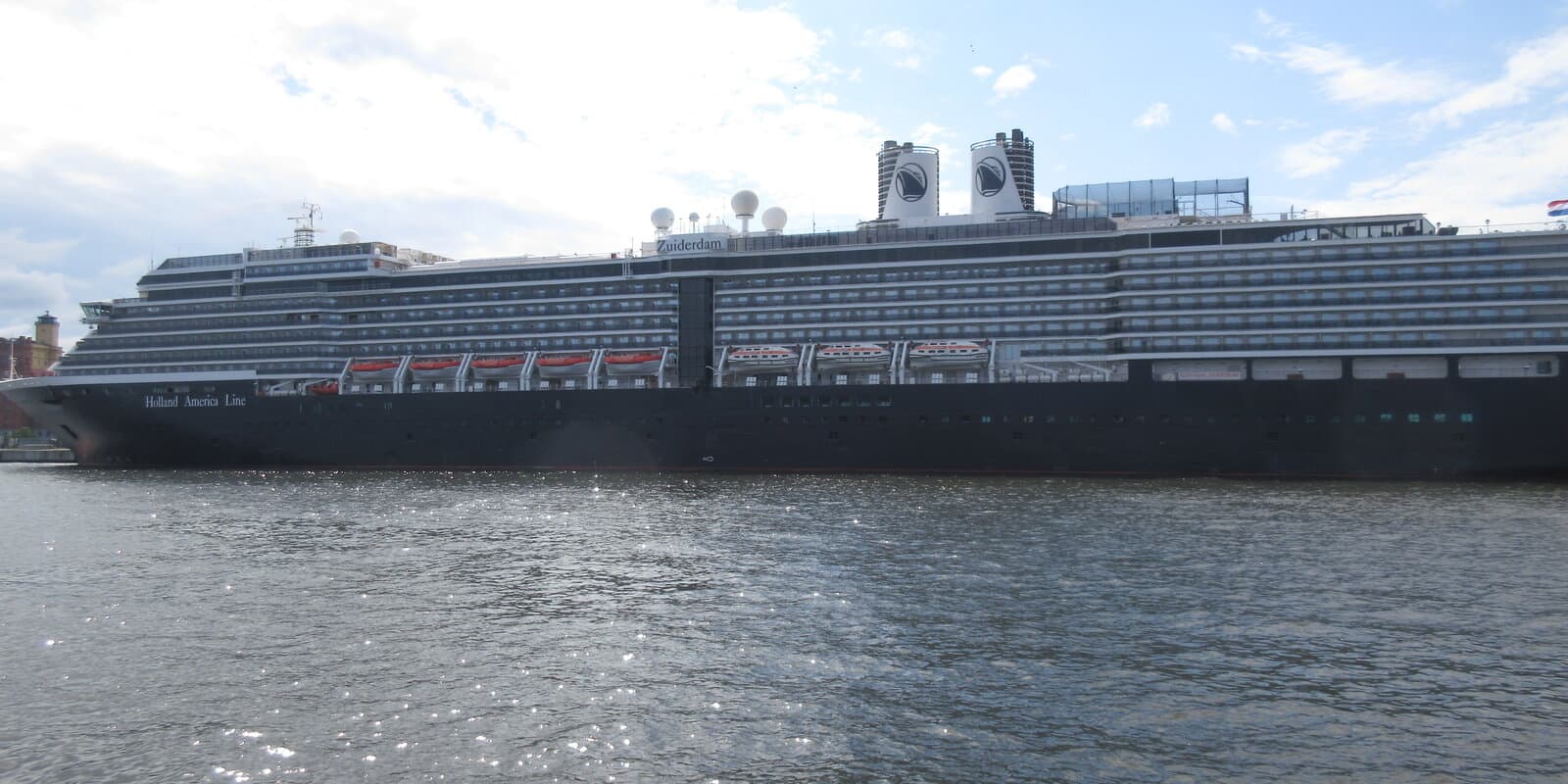 Holland America Line MS Zuiderdam in profile at a European harbor, dark hull with white superstructure, ship name visible on the upper decks