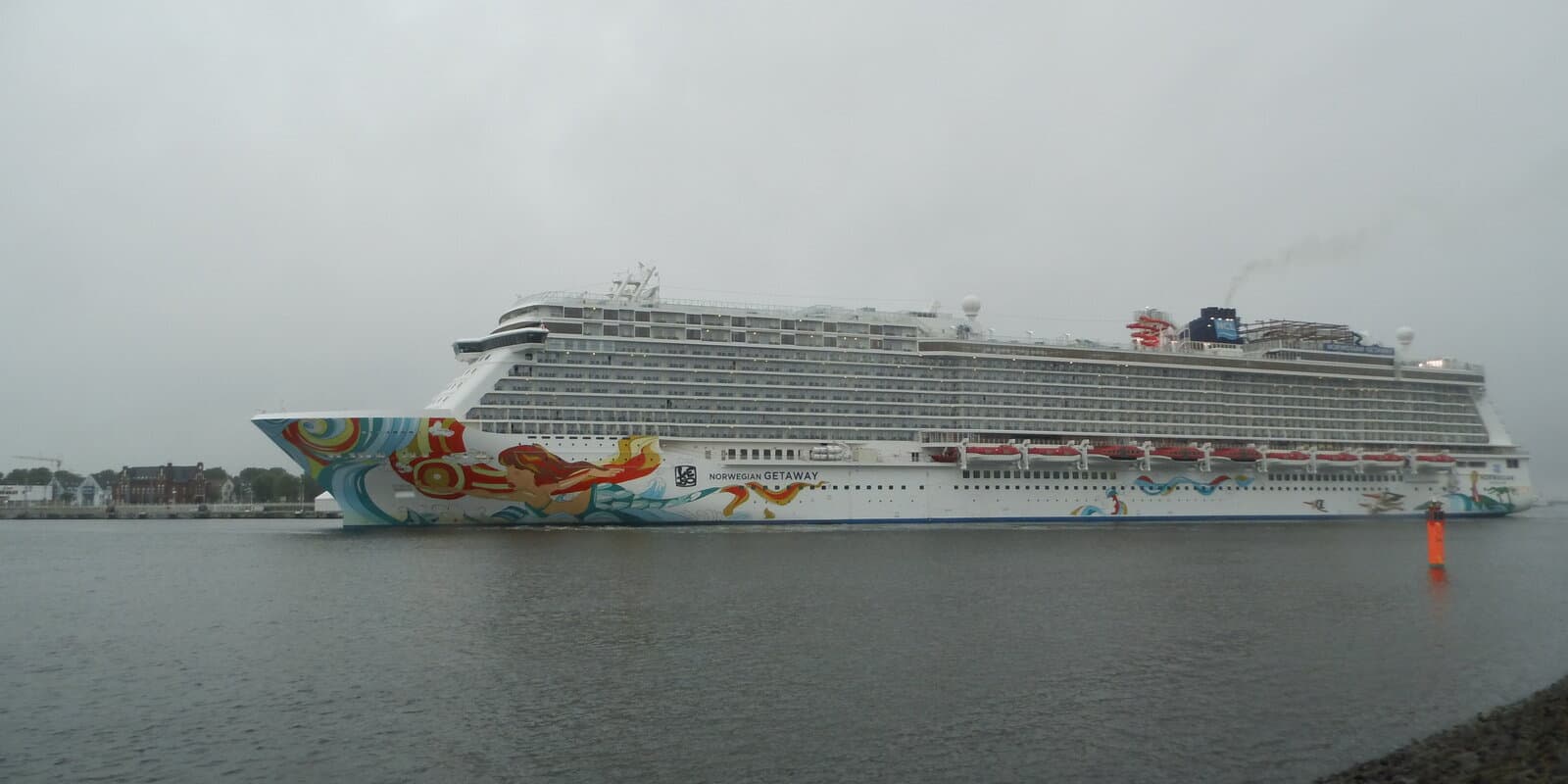 Norwegian Getaway cruise ship in side profile underway on gray water under an overcast sky, with colorful mermaid hull art and the name NORWEGIAN GETAWAY on the bow