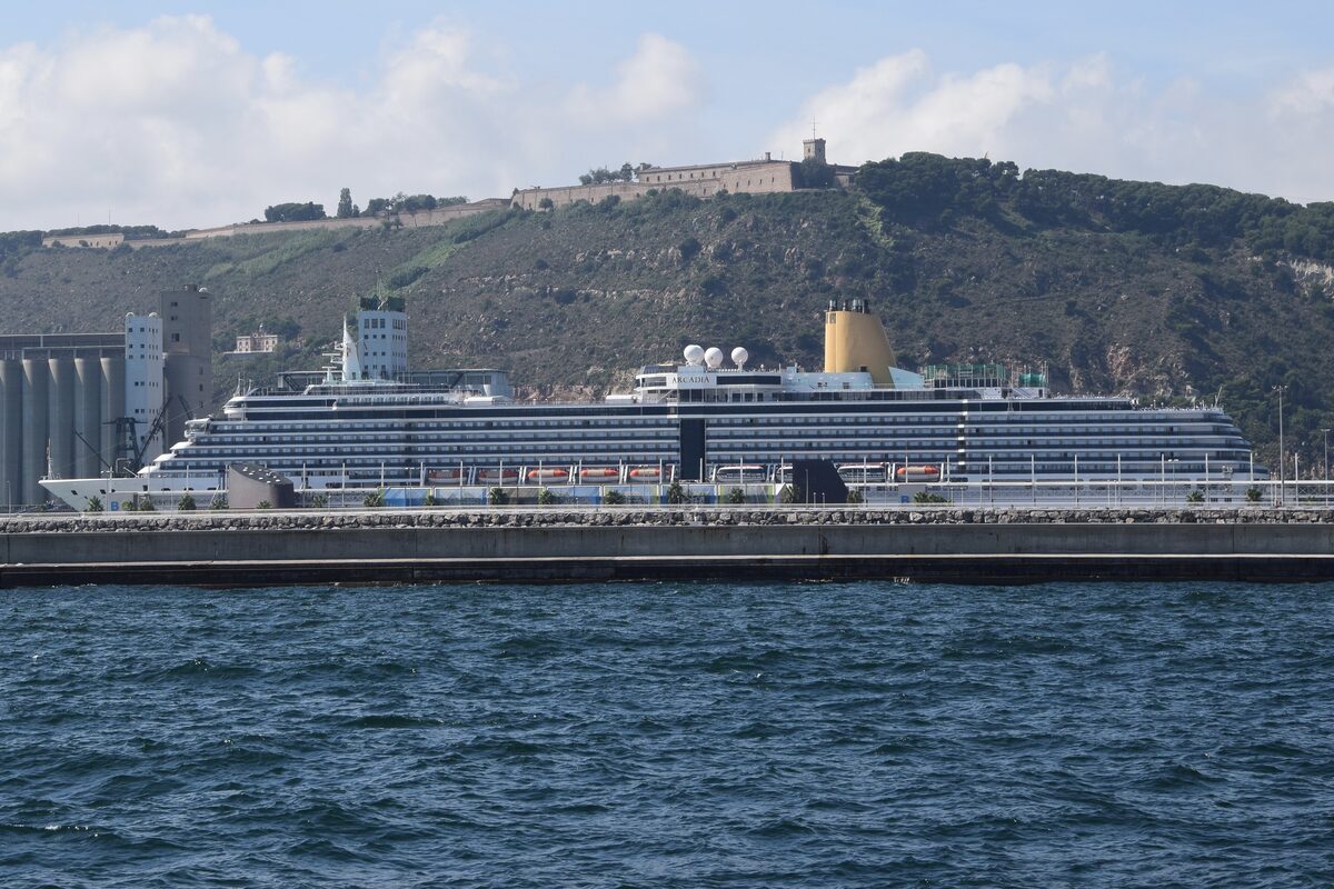 A cruise ship berthed at the Port of Barcelona terminal with city skyline in the background