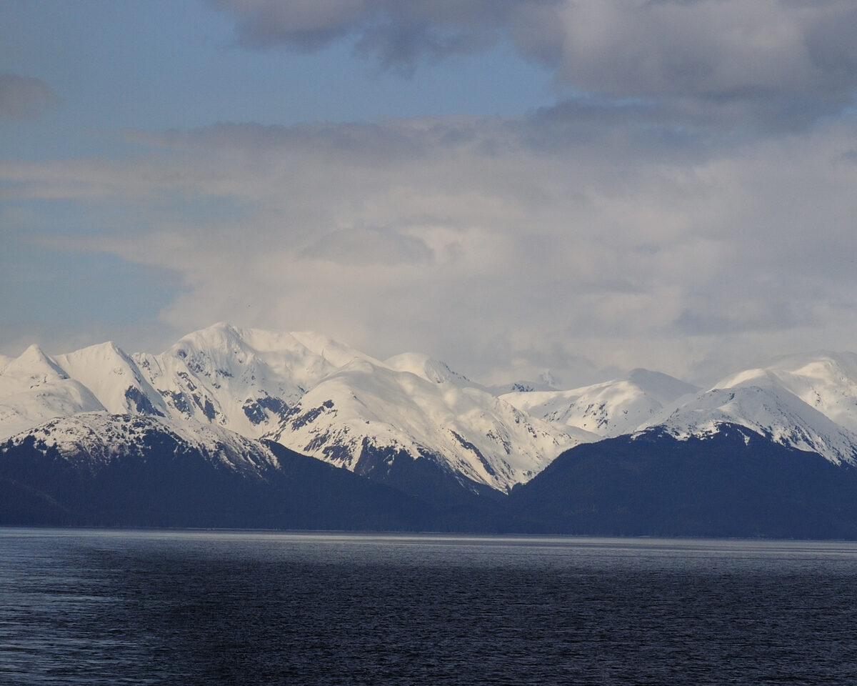 Calm blue water in a steep-walled Alaska fjord with forested mountains rising on both sides