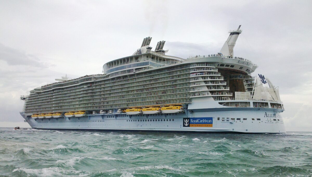 Allure of the Seas cruise ship departing Port Everglades channel with port infrastructure visible along the waterway