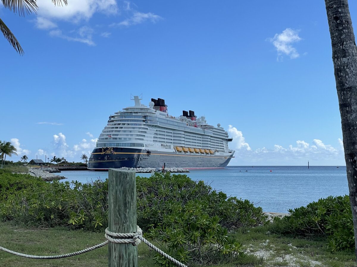 Disney Wish cruise ship docked at Castaway Cay with turquoise water and tropical bushes in the foreground