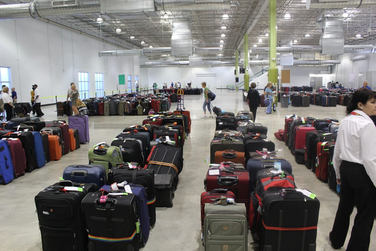 Rows of suitcases on the floor inside a cruise terminal baggage hall with passengers walking nearby