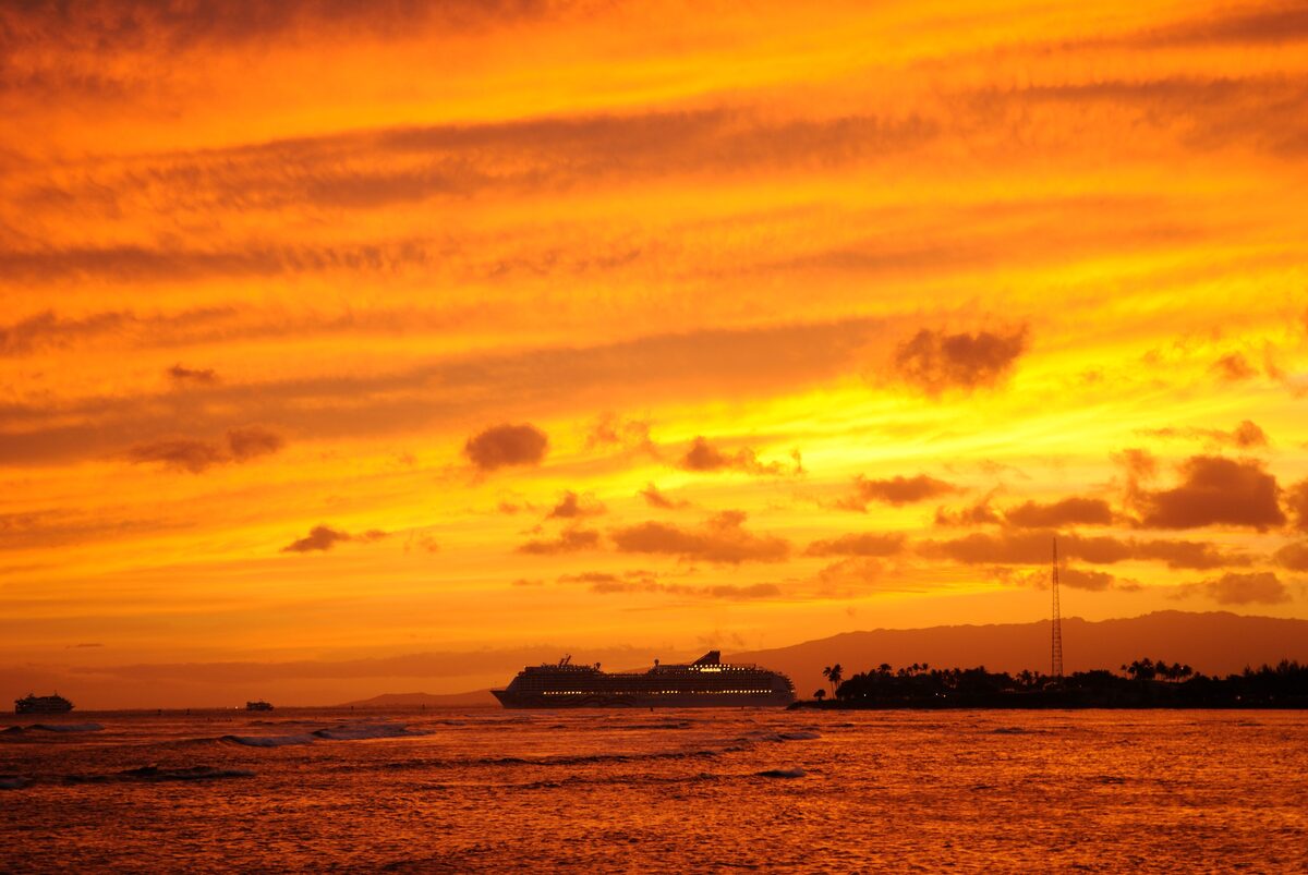Pride of America cruise ship silhouetted against an orange sunset while departing Honolulu Harbor