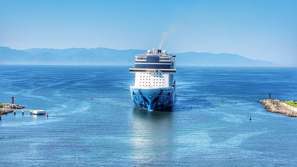 Norwegian Bliss cruise ship entering a harbor channel with green hills along the Mexican Riviera coast