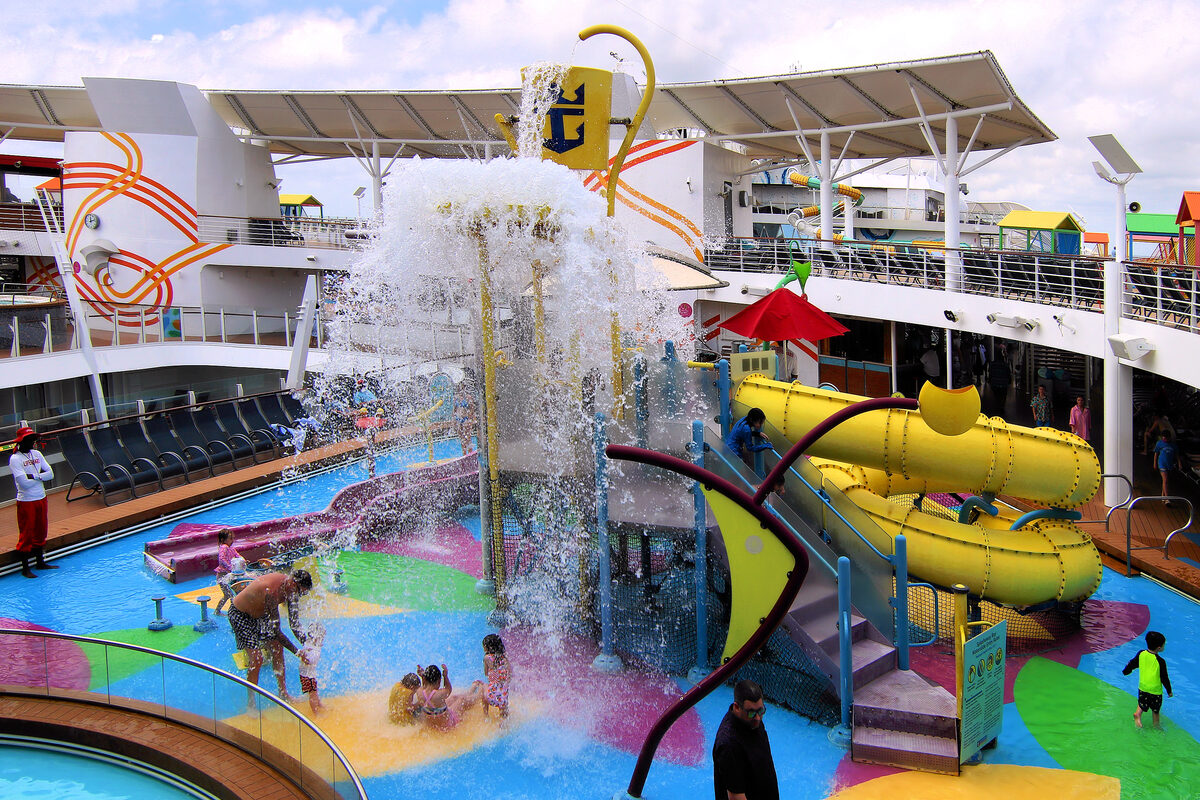 Splashaway Bay water playground on Royal Caribbean's Harmony of the Seas with children playing under a tipping bucket and yellow spiral slide