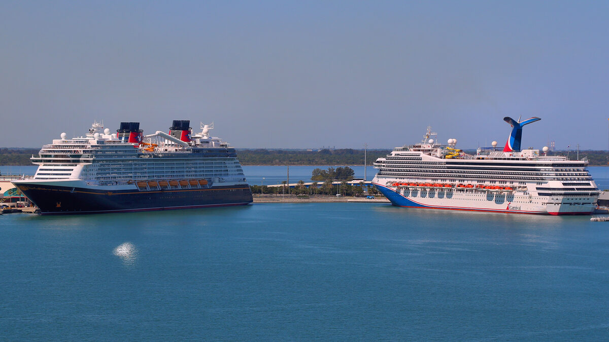 Disney Cruise Line ship and Carnival Freedom docked at Port Canaveral with calm blue harbor water in the foreground