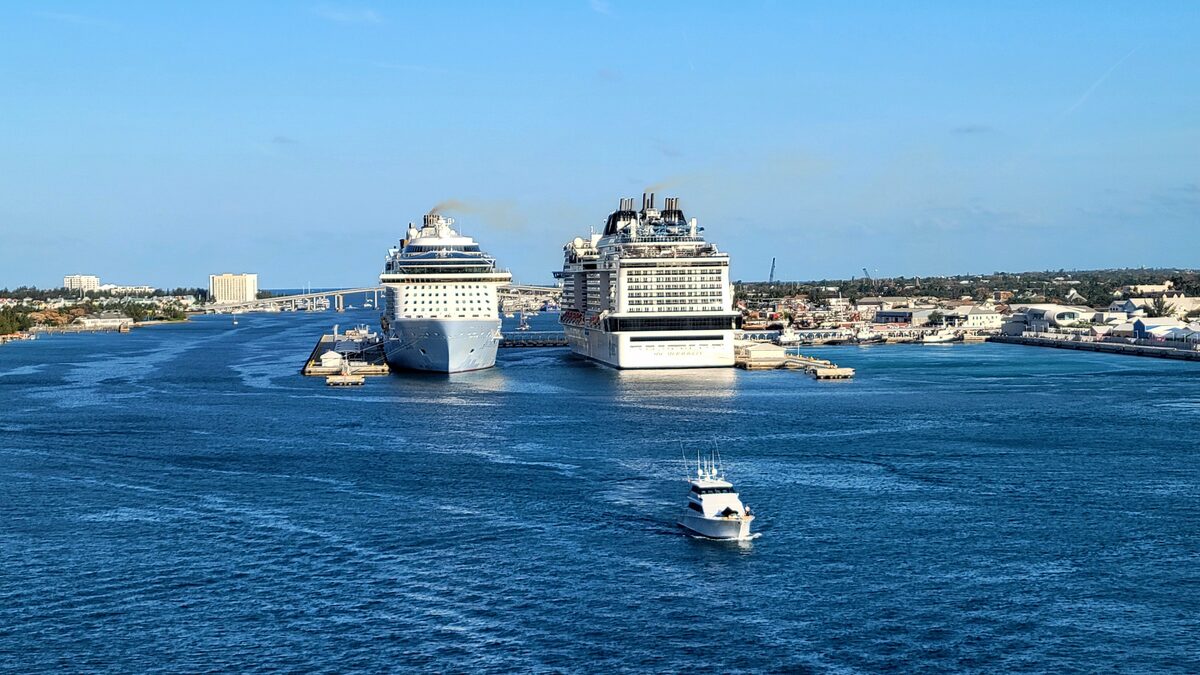 Two cruise ships docked at Nassau Cruise Port in the Bahamas under clear blue sky, with a small motorboat in the harbor